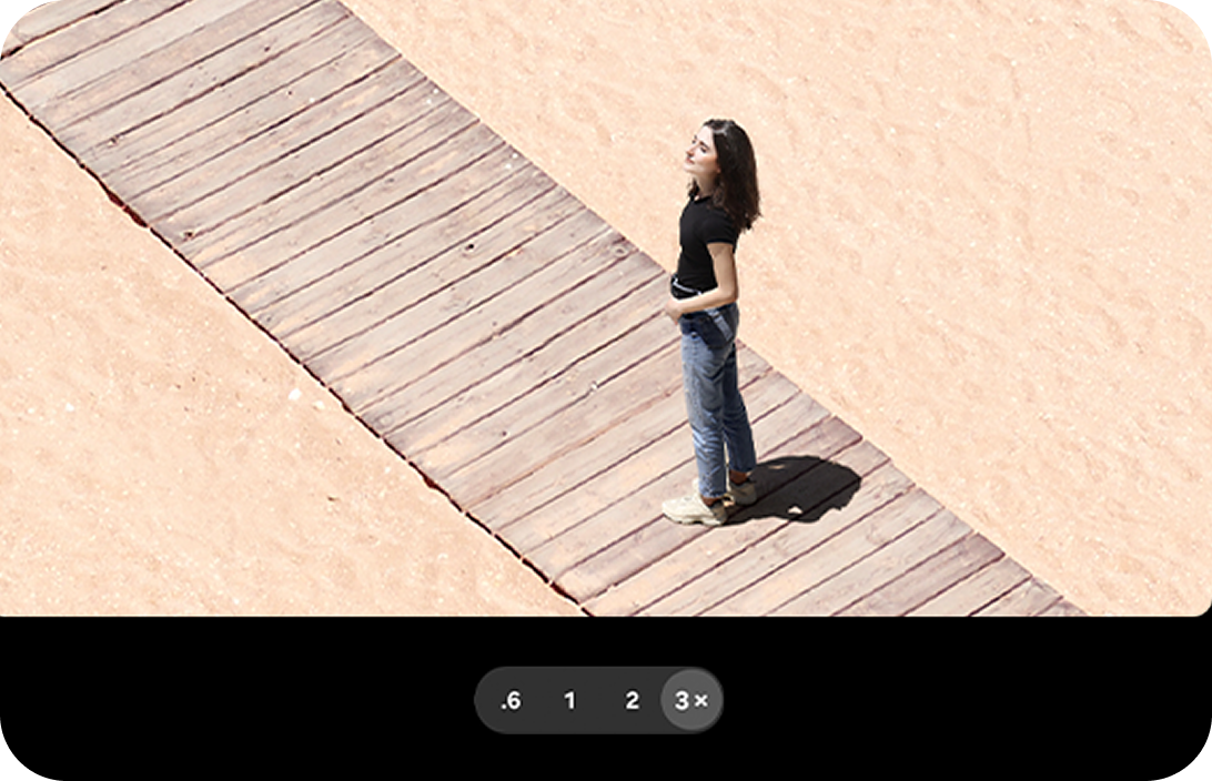 A woman standing on a beach walkway, zoomed into the 3x option.